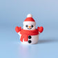 May include: A small snowman figure with a red hat, scarf, and mittens. The snowman has a smiling face with black eyes and a carrot nose. Two black buttons are on the snowman's body. The background is a light blue.